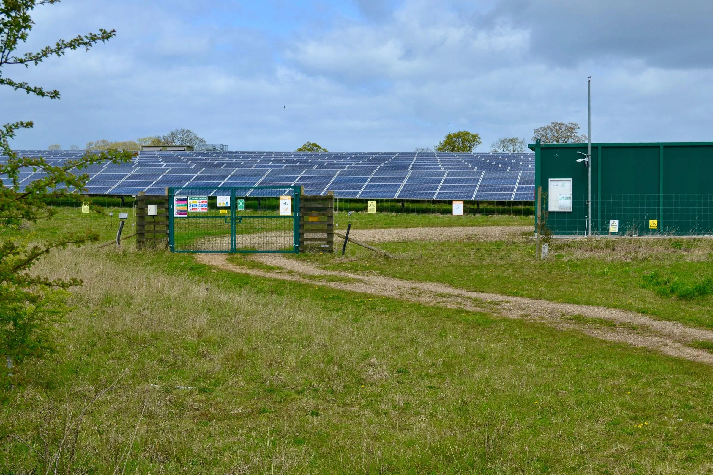 Campo fotovoltaico con file di pannelli solari e una cabina tecnica sotto un cielo nuvoloso