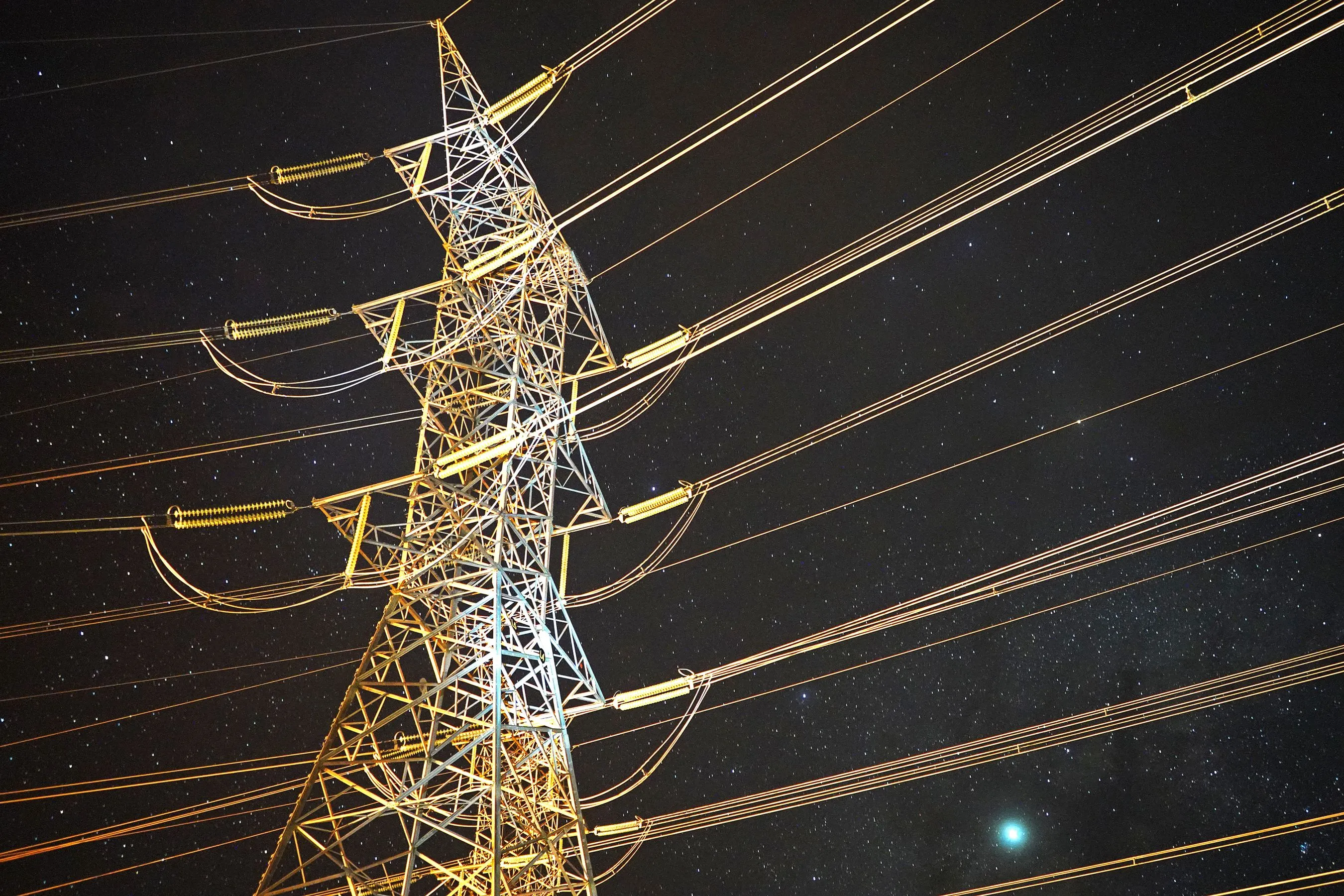 High-voltage pylon at night, under a starry sky