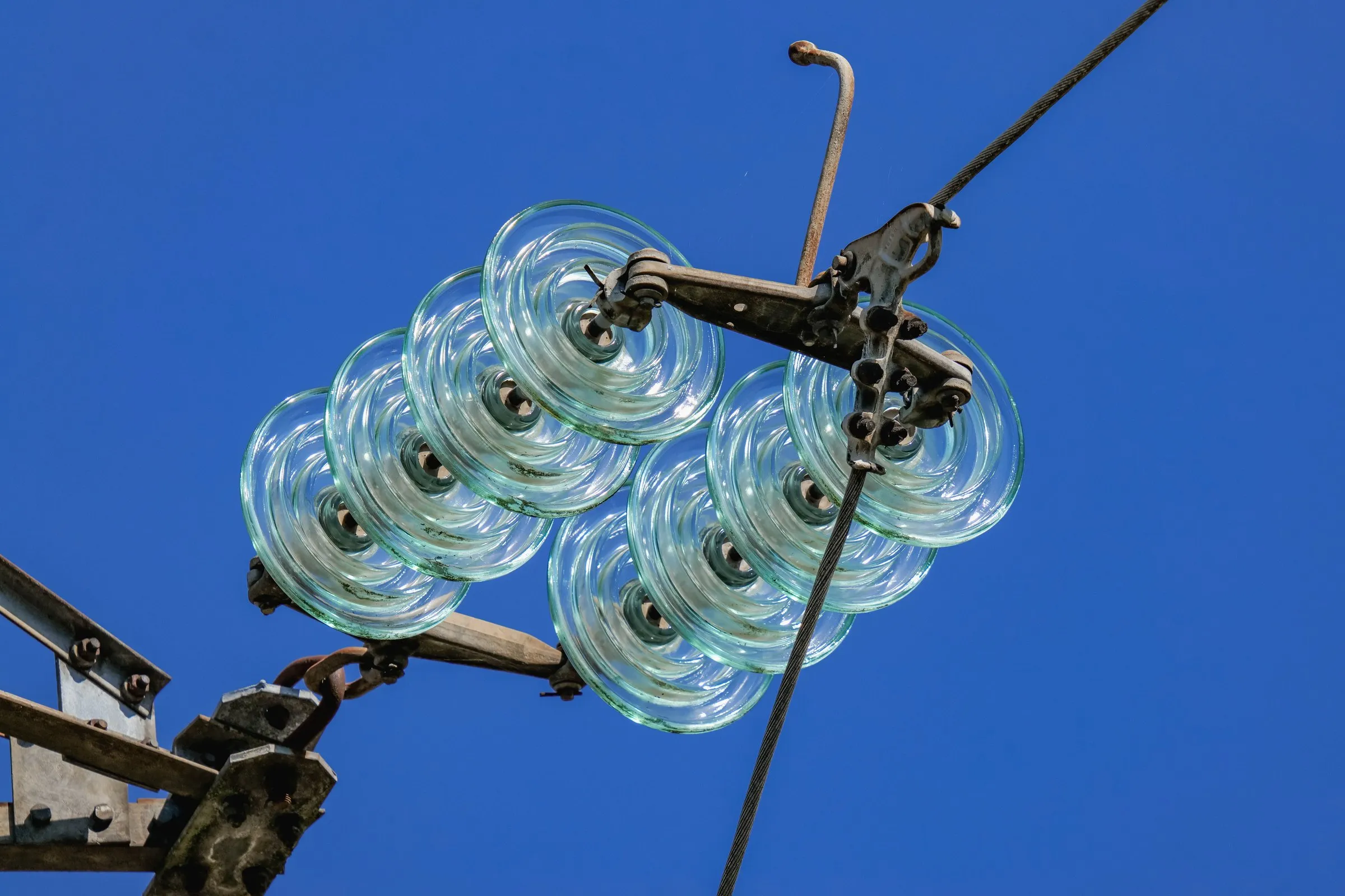 Catena di isolatori in vetro sospesa su una linea ad alta tensione contro un cielo blu intenso